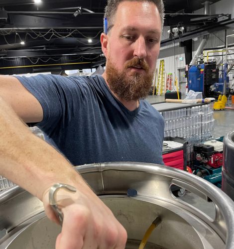 Stephen Vukovics brewing beer. Stirring mash in metal pot for beer.